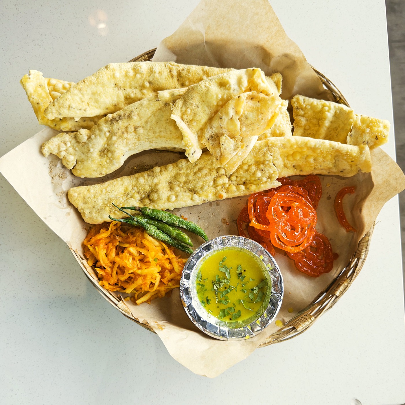 A basket of fafda and jalebi with chutney, sambharo and fried chillies